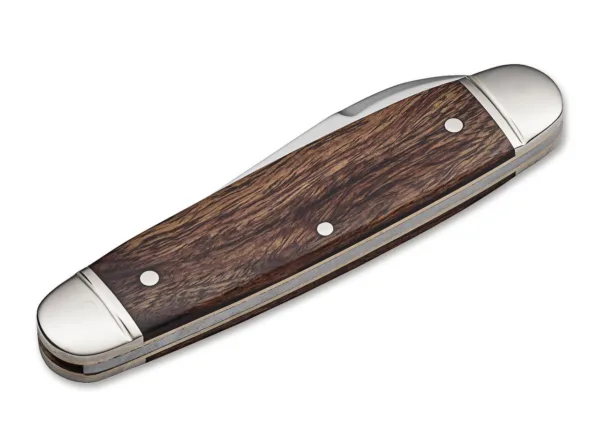 Nóż Böker Club Knife Gentleman Das traditionelle Böker Club Knife ist der elegante Bruder des berühmten Böker Sportmessers, das in Nordamerika als Camp Knife bekannt ist. Bei fast gleichen Abmessungen ist die Formgebung allerdings durchgehend und wird nicht durch Aussparungen für die Werkzeuge unterbrochen. Der charakteristische Metallbügel zur Befestigung einer Messerkette fehlt beim Club Knife ebenfalls. Der Erl der Neuauflage dieses historischen Gentlemanmessers besteht aus Messing, während die dekorativen Backen aus Neusilber gefertigt werden und mit einer fein gefrästen Nut verziert sind. Für die Griffschalen wird reizvoll gemasertes Wüsteneisenholz aus zertifiziertem Import verwendet. Die Klinge mit historischer Formgebung wird aus N690 gefertigt und verriegelt nicht. Der lange Nagelhau, auch Long Pull genannt, ist mit einer feinen Zahnung versehen und erlaubt so das Entzünden von geeigneten Streichhölzern. Die Auslieferung des komplett von Hand in der Böker Manufaktur Solingen gefertigten Slipjoint-Messers erfolgt mit dem neu aufgelegten historischen Böker Baumzeichen-Emblem.