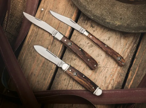 Nóż Böker Club Knife Gentleman Das traditionelle Böker Club Knife ist der elegante Bruder des berühmten Böker Sportmessers, das in Nordamerika als Camp Knife bekannt ist. Bei fast gleichen Abmessungen ist die Formgebung allerdings durchgehend und wird nicht durch Aussparungen für die Werkzeuge unterbrochen. Der charakteristische Metallbügel zur Befestigung einer Messerkette fehlt beim Club Knife ebenfalls. Der Erl der Neuauflage dieses historischen Gentlemanmessers besteht aus Messing, während die dekorativen Backen aus Neusilber gefertigt werden und mit einer fein gefrästen Nut verziert sind. Für die Griffschalen wird reizvoll gemasertes Wüsteneisenholz aus zertifiziertem Import verwendet. Die Klinge mit historischer Formgebung wird aus N690 gefertigt und verriegelt nicht. Der lange Nagelhau, auch Long Pull genannt, ist mit einer feinen Zahnung versehen und erlaubt so das Entzünden von geeigneten Streichhölzern. Die Auslieferung des komplett von Hand in der Böker Manufaktur Solingen gefertigten Slipjoint-Messers erfolgt mit dem neu aufgelegten historischen Böker Baumzeichen-Emblem.