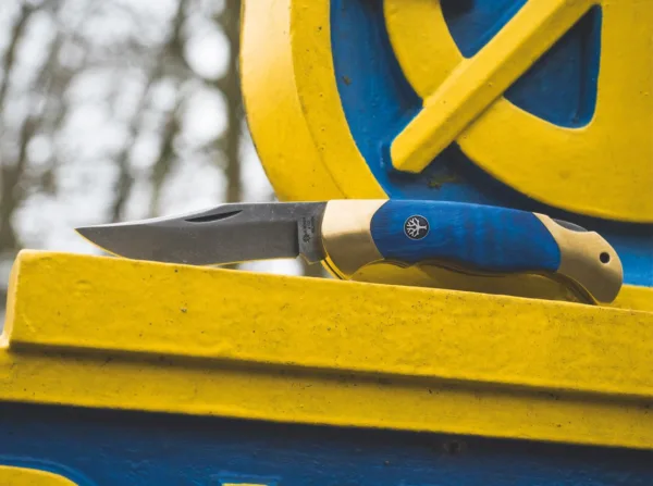 Nóż Böker Scout Solingen Während der Feierlichkeiten anlässlich des 150-jährigen Jubiläums der Böker Manufaktur fragte uns der Oberbürgermeister der Stadt Solingen, ob wir ein hochwertiges Taschenmesser in den Farben der Stadt entwickeln könnten. Er würde sich sehr freuen, ein solches Messer zu offiziellen Anlässen an Gäste überreichen zu können. Diese Anfrage ehrte uns sehr und schnell fiel die Wahl für das Grundmodell auf das überaus beliebte und vielseitige Böker Scout. Seit über dreißig Jahren überzeugt das Scout mit seiner eleganten und zeitlosen Formgebung sowie seiner stabilen und ergonomischen Bauweise mit gesintertem Griffkörper Messerfreunde auf der ganzen Welt. Die Farben der Stadt Solingen sind ein kräftiges Stahlblau und Goldgelb. Statt mit einem gesinterten Körper aus Neusilber wird das Scout Solingen erstmalig mit einem Körper aus massivem Messing ausgestattet, der präzise per CNC-Technik aus dem Vollen gefräst wird. In Anlehnung an den gewaltigen Kastanienbaum vor der ersten Böker Handwerkzeug-Fabrik, haben wir uns für Griffschalen aus blau stabilisiertem Holz der Rosskastanie entschieden. Um die jahrhundertealte Tradition der Klingenstadt Solingen zu betonen, wird die Klinge aus nicht rostfreiem C75 Kohlenstoffstahl gefertigt und mit einem authentischen Acid Wash Finish versehen. Die Auslieferung des komplett von Hand in der Böker Manufaktur Solingen gefertigten Messers erfolgt mit dem neu aufgelegten historischen Böker Baumzeichen-Emblem. Zudem möchten wir mit diesem besonderen Messer ein altes Solinger Ritual wiederaufleben lassen. Messer sind ein perfektes Präsent, über das sich fast jeder freut. Allerdings sagt der Volksmund in der Klingenstadt, dass ein verschenktes Messer das Band der Freundschaft zerschneidet. Um dieses Unglück zu verhindern, erhält der Beschenkte mit dem Messer eine Geldmünze, die er dem Schenker wieder zurückgibt. Dem Brauchtum folgend wurde das Messer so bezahlt und gilt nicht länger als unglücksverheißendes Geschenk. Damit das Böker Scout Solingen in Zukunft viele Freundschaften begründen und erhalten kann, wird jedes Messer daher mit einer praktischen Böker Münze ausgeliefert.