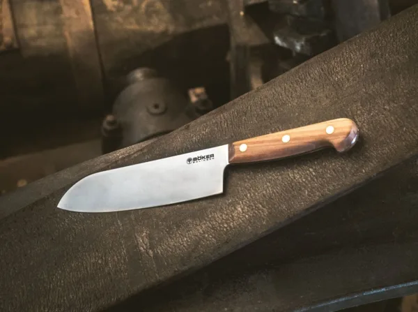 Nóż Santoku Böker Solingen Cottage-Craft Tak zwani Kotten kształtują historię miasta Solingen od XIV wieku. Masywne osełki napędzane były czystą wodą, a słynne na całym świecie ostrza szlifowano ręcznie. Seria noży szefa kuchni Böker Cottage-Craft imponująco kontynuuje dziedzictwo tego tradycyjnego rzemiosła i zachwyca starannie dobranym wyborem klasycznych materiałów. Na szczególną uwagę zasługuje zastosowanie rdzewnej stali węglowej C75, która po krótkim okresie użytkowania tworzy typową niebiesko-szarą patynę. Naturalne drewno śliwkowe użyte do wykonania muszli rękojeści jest twarde, gęste i drobnoporowate, ma jednolitą strukturę i uderzające spektrum kolorów. Zgodnie z wielowiekową tradycją produkcji noży z Solingen, łuski rękojeści są mocowane na ciągłym trzpieniu ostrza za pomocą nitów z litego mosiądzu.Nóż, który staje się coraz bardziej popularny w Europie, to Santoku. Pierwotnie był to japoński kształt ostrza noża użytkowego. W tłumaczeniu jego nazwa oznacza „Trzy cnoty” i nadaje się równie dobrze do mięsa, ryb i warzyw. Dzięki szerokiemu ostrzu Santoku jest szczególnie łatwy w obsłudze.CARBON STEEL C75 Całkowicie naturalną właściwością materiału jest to, że podczas używania noża powstaje patyna. Szaroniebieskie zmatowienie ostrza jest całkowicie normalne i nie jest w żaden sposób wadą. Wręcz przeciwnie, powstała w ten sposób patyna (warstwa tlenku) tworzy na ostrzu warstwę ochronną, która zwiększa jego odporność na warunki zewnętrzne. Ta patyna jest często widoczna już po pierwszym użyciu i nie można jej ponownie usunąć. Ekspert natychmiast rozpoznaje wynikającą z tego wysokiej jakości stal węglową. Przy odpowiedniej pielęgnacji stal węglowa ma taką samą żywotność jak nowoczesna stal nierdzewna. CZYSZCZENIE I PIELĘGNACJA Stal węglowa jest jednym z rdzewnych rodzajów stali i wymaga celowej, ale minimalnej konserwacji. W kuchni wystarczy opłukać nóż pod gorącą bieżącą wodą i osuszyć ściereczką. W przypadku dłuższego przechowywania ostrze należy konserwować odpowiednim olejem. Idealny do tego celu jest bezkwasowy, nieżywiczny i nielotny olej Boker Camellia (nr kat. 04BO175). Jest olejem czysto roślinnym i idealnie nadaje się do konserwacji rdzewnych noży kuchennych, w przeciwieństwie do innych olejów pielęgnacyjnych – nie tworzy emulsji z wodą. Z drugiej strony, używanie zmywarki niszczy drobne struktury stali węglowej, podobnie jak pozostawianie ostrza w zlewie na dłuższy czas bez czyszczenia. Rzadko stosowana w nożach kuchennych stal węglowa, ze względu na swoje właściwości można ją łatwo ostrzyć, dzięki czemu noże Boker Cottage Craft stają się lojalnymi i niezawodnymi towarzyszami na całe życie i kontynuują pisanie własnej historii.