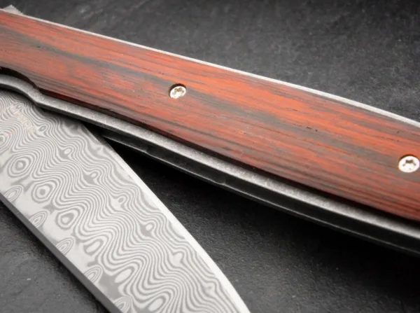 Nóż Böker Plus Urban Trapper Cocobolo Damascus Oryginalny model Boker Plus Urban Trapper autorstwa Brada Zinkera szybko stał się jednym z najpopularniejszych noży dżentelmeńskich w naszej ofercie i jest dostarczany z ostrzem wykonanym ze stali damasceńskiej nierdzewnej w szczególnie eleganckiej wersji kolekcjonerskiej. Niezwykle płaska i bardzo smukła konstrukcja sprawia, że Urban Trapper jest niezrównanym nożem składanym z wyższej półki. Głownia ze 110 warstw damastu zamocowana jest na łożyskach klulkowych, otwierana za pomocą flippera i bezpiecznie blokowana niezawodnym linerlockiem. Lekka rękojeść wykonana jest z tytanu z okładkami wykonanymi z klasycznego drewna cocobolo, które z jednej strony zapewniają nieco pełniejszy chwyt, a z drugiej - wyjątkowy wygląd. Przepiękna struktura czerwonawego drewna nawiązuje do marmuru, a dzięki wyjątkowo dużej zawartości olejków ma również intensywny kwiatowy zapach. Dostarczany z odpinanym klipsem do przenoszenia (tip-up/r) wykonanym z tytanu i wysokiej jakości nylonowym etui do przechowywania.