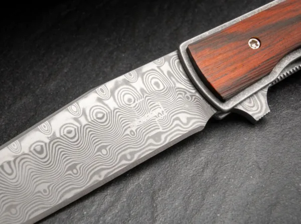 Nóż Böker Plus Urban Trapper Cocobolo Damascus Oryginalny model Boker Plus Urban Trapper autorstwa Brada Zinkera szybko stał się jednym z najpopularniejszych noży dżentelmeńskich w naszej ofercie i jest dostarczany z ostrzem wykonanym ze stali damasceńskiej nierdzewnej w szczególnie eleganckiej wersji kolekcjonerskiej. Niezwykle płaska i bardzo smukła konstrukcja sprawia, że Urban Trapper jest niezrównanym nożem składanym z wyższej półki. Głownia ze 110 warstw damastu zamocowana jest na łożyskach klulkowych, otwierana za pomocą flippera i bezpiecznie blokowana niezawodnym linerlockiem. Lekka rękojeść wykonana jest z tytanu z okładkami wykonanymi z klasycznego drewna cocobolo, które z jednej strony zapewniają nieco pełniejszy chwyt, a z drugiej - wyjątkowy wygląd. Przepiękna struktura czerwonawego drewna nawiązuje do marmuru, a dzięki wyjątkowo dużej zawartości olejków ma również intensywny kwiatowy zapach. Dostarczany z odpinanym klipsem do przenoszenia (tip-up/r) wykonanym z tytanu i wysokiej jakości nylonowym etui do przechowywania.