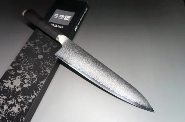 Shizu Hamono MIYAKO Japoński nóż szefa kuchni damast 21cm AUS-8 Shizu Hamono Bessaku Miyako Damascus  Nóż Szefa Kuchni 21cm   Nóż Shizu Hamono Bessaku Miyako 21cm to idealne narzędzie dla profesjonalnych kucharzy i miłośników gotowania. Dzięki temu nożowi z łatwością posiekasz mięso, zioła i warzywa. Nie używaj go jednak do krojenia bardzo twardych lub zamrożonych produktów. Cechy Ostrza: Stal Damaskowana: Rdzeń ze stali AUS8, wzbogacony molibdenem i wanadem, otoczony warstwami SUS410 Skład Stopu: 0,8% węgla dla twardości, 14,5% chromu dla odporności na korozję. Wytrzymałość: AUS8 to idealny kompromis między twardością a elastycznością. Unikalne Cechy: Warstwy SUS410: Zwiększają wytrzymałość i równowagę ostrza. Młotkowanie Ostrza: Dodatkowy charakter i unikalny wygląd. Rękojeść: Laminowane drewno, polerowane dla komfortu, tradycyjny japoński kształt "D". Szczegóły Produktu: Producent: Shizu Hamono Co.,Ltd. (Japonia) Stal Ostrza: 33-warstwowa stal damasceńska, rdzeń AUS8 Twardość: 59 HRC Rękojeść: Laminowane drewno, stalowa nasadka Typ: Nóż Gyuto Długość Ostrza: 210 mm Długość Całkowita: 342 mm Waga: 173 g Krawędź: Dwustronna (50/50) Kraj Produkcji: Japonia