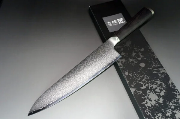 Shizu Hamono MIYAKO Japoński nóż szefa kuchni damast 21cm AUS-8 Shizu Hamono Bessaku Miyako Damascus  Nóż Szefa Kuchni 21cm   Nóż Shizu Hamono Bessaku Miyako 21cm to idealne narzędzie dla profesjonalnych kucharzy i miłośników gotowania. Dzięki temu nożowi z łatwością posiekasz mięso, zioła i warzywa. Nie używaj go jednak do krojenia bardzo twardych lub zamrożonych produktów. Cechy Ostrza: Stal Damaskowana: Rdzeń ze stali AUS8, wzbogacony molibdenem i wanadem, otoczony warstwami SUS410 Skład Stopu: 0,8% węgla dla twardości, 14,5% chromu dla odporności na korozję. Wytrzymałość: AUS8 to idealny kompromis między twardością a elastycznością. Unikalne Cechy: Warstwy SUS410: Zwiększają wytrzymałość i równowagę ostrza. Młotkowanie Ostrza: Dodatkowy charakter i unikalny wygląd. Rękojeść: Laminowane drewno, polerowane dla komfortu, tradycyjny japoński kształt "D". Szczegóły Produktu: Producent: Shizu Hamono Co.,Ltd. (Japonia) Stal Ostrza: 33-warstwowa stal damasceńska, rdzeń AUS8 Twardość: 59 HRC Rękojeść: Laminowane drewno, stalowa nasadka Typ: Nóż Gyuto Długość Ostrza: 210 mm Długość Całkowita: 342 mm Waga: 173 g Krawędź: Dwustronna (50/50) Kraj Produkcji: Japonia