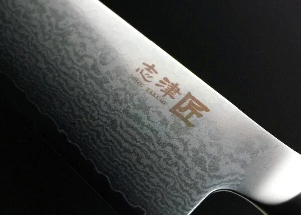 Shizu Hamono MIYAKO Japoński nóż szefa kuchni damast 21cm AUS-8 Shizu Hamono Bessaku Miyako Damascus  Nóż Szefa Kuchni 21cm   Nóż Shizu Hamono Bessaku Miyako 21cm to idealne narzędzie dla profesjonalnych kucharzy i miłośników gotowania. Dzięki temu nożowi z łatwością posiekasz mięso, zioła i warzywa. Nie używaj go jednak do krojenia bardzo twardych lub zamrożonych produktów. Cechy Ostrza: Stal Damaskowana: Rdzeń ze stali AUS8, wzbogacony molibdenem i wanadem, otoczony warstwami SUS410 Skład Stopu: 0,8% węgla dla twardości, 14,5% chromu dla odporności na korozję. Wytrzymałość: AUS8 to idealny kompromis między twardością a elastycznością. Unikalne Cechy: Warstwy SUS410: Zwiększają wytrzymałość i równowagę ostrza. Młotkowanie Ostrza: Dodatkowy charakter i unikalny wygląd. Rękojeść: Laminowane drewno, polerowane dla komfortu, tradycyjny japoński kształt "D". Szczegóły Produktu: Producent: Shizu Hamono Co.,Ltd. (Japonia) Stal Ostrza: 33-warstwowa stal damasceńska, rdzeń AUS8 Twardość: 59 HRC Rękojeść: Laminowane drewno, stalowa nasadka Typ: Nóż Gyuto Długość Ostrza: 210 mm Długość Całkowita: 342 mm Waga: 173 g Krawędź: Dwustronna (50/50) Kraj Produkcji: Japonia